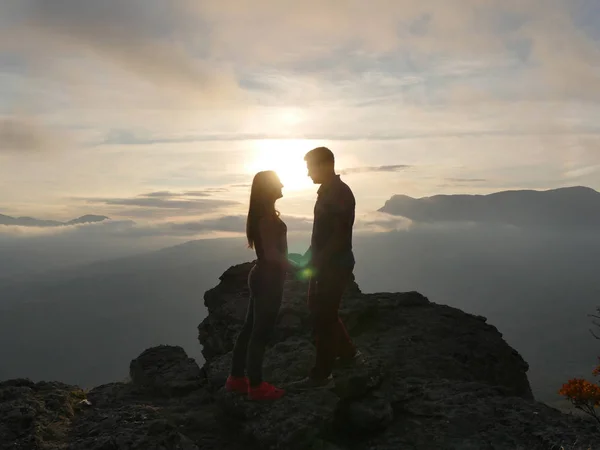 Siluetas de pareja joven de pie en una montaña y mirando el uno al otro en el hermoso fondo del atardecer. Amor de chico y chica . —  Fotos de Stock