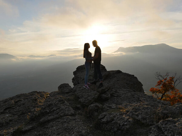 Silhouettes of young couple standing on a mountain and looking to each other on beautiful sunset background. Love of guy and girl.