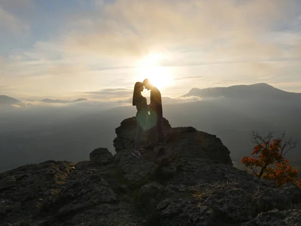 Siluetas de pareja joven de pie en una montaña y mirando el uno al otro en el hermoso fondo del atardecer. Amor de chico y chica . —  Fotos de Stock