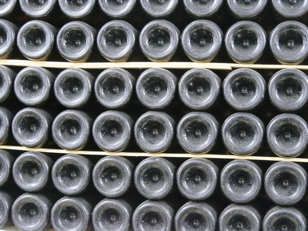 Old bottles of wine in rows in wine cellar. Rows of many wine bottles in winery cellar storage. Beautiful texture or background. Close up