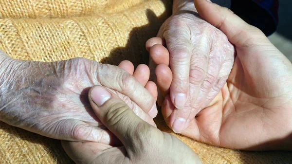 Un giovane maschio mani confortante un anziano paio di mani della nonna all'aperto da vicino . — Foto Stock