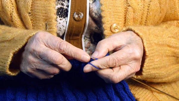 De oude vrouw zit thuis en breit kleding — Stockfoto