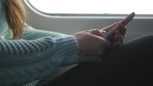 Chica joven viajando en un tren y utilizando el teléfono móvil. Hermosa mujer envía un mensaje desde el teléfono inteligente. Chica atractiva charlando con amigos — Vídeo de stock