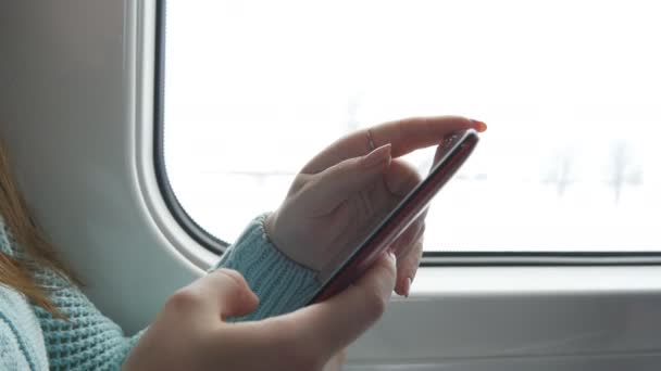 Mujer joven viajando en un tren y utilizando el teléfono móvil. La mano femenina envía un mensaje desde el teléfono inteligente. Brazo de chica charlando con amigos. De cerca. — Vídeos de Stock