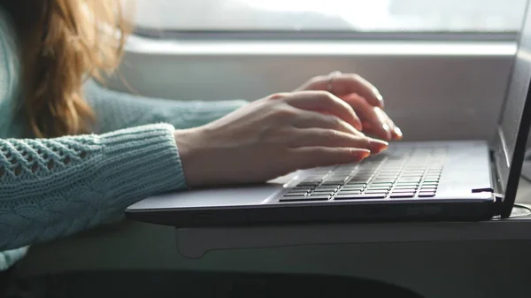 Female hands typing on keyboard of laptop in train. Woman chatting with friends during traveling on railway. Young girl using notebook. Arm print a message. Close up — Stock Photo, Image