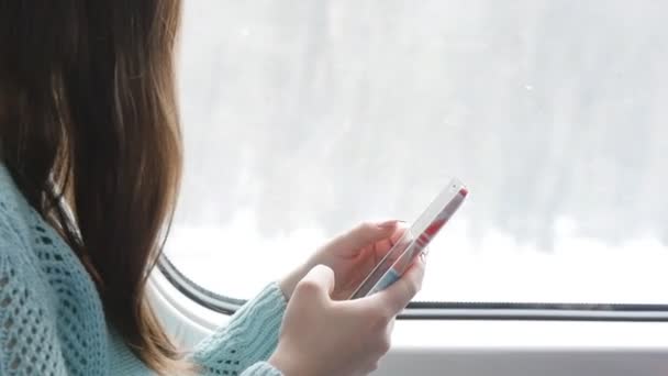 Молода дівчина подорожує потягом і використовує мобільний телефон. Красива жінка надсилає повідомлення зі смартфона. Жіночі руки спілкуються з друзями. Крупним планом Повільний рух — стокове відео