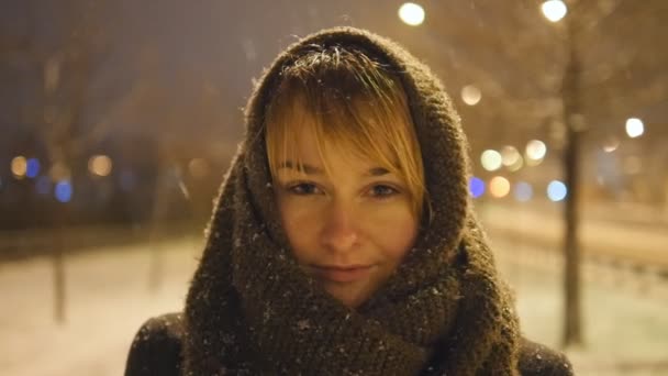 Портрет привлекательной женщины, смотрящей в камеру в зимнее время на открытом воздухе. Молодая девушка стоит на улице и наслаждается снегопадом в замедленной съемке с миганием — стоковое видео