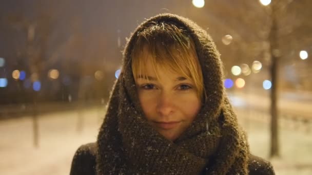 Portrait of attractive woman looking at camera at winter time outdoor. Young girl stands on the street, and enjoys the snowfall in slow motion. Close up — Stock Video