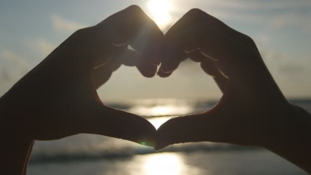 Ragazza che fa cuore con le mani sul fondo del mare con un bel tramonto dorato. Silhouette del braccio femminile a forma di cuore con alba all'interno. Concetto di vacanza. Vacanze estive sulla spiaggia — Video Stock