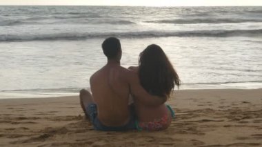 Genç Romantik Çift sahilde oturan ve sarılma harika bir manzara keyif alıyor. Bir kadın ve bir adam oturuyor birlikte sahil üzerinde kum okyanus ve manzara hayran. Yakın çekim