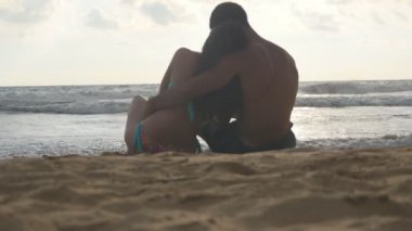 Genç Romantik Çift sahilde oturan ve sarılma harika bir manzara keyif alıyor. Bir kadın ve bir adam oturuyor birlikte sahil üzerinde kum okyanus ve manzara hayran. Yakın çekim
