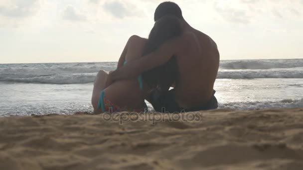 Genç Romantik Çift sahilde oturan ve sarılma harika bir manzara keyif alıyor. Bir kadın ve bir adam oturuyor birlikte sahil üzerinde kum okyanus ve manzara hayran. Yakın çekim — Stok video