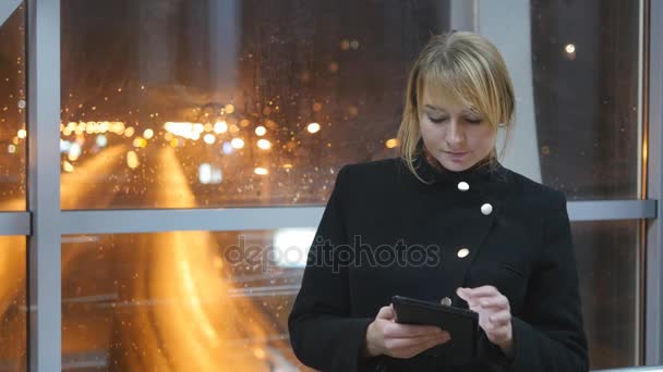 Jovem mulher usar comprimido à noite no interior. Retrato de menina atraente com tablet nas mãos. Fecha. Belo embaçamento noite tráfego da cidade na janela no fundo — Vídeo de Stock