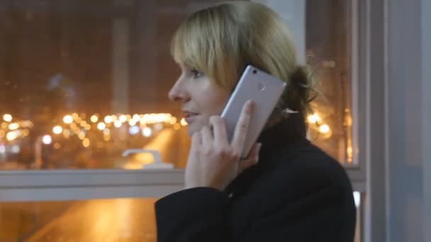Mujer joven hablando por teléfono y caminando en el interior de la noche. Una chica atractiva hablando por celular. De cerca. — Vídeo de stock