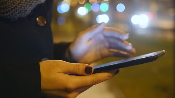 年轻的女孩在晚上使用 tablet pc 在户外在城市。美丽的模糊背景在夜城市交通。关闭 — 图库视频影像