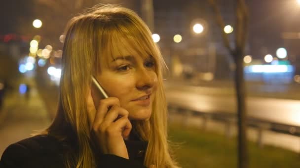 Junge Frau telefoniert am Abend im Freien. Porträt eines attraktiven Mädchens, das mit dem Handy spricht. Nahaufnahme. schöne verschwommene Nacht Stadt im Hintergrund — Stockvideo