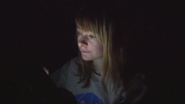 Genç yakışıklı sarışın kız evi onun ışıkları yatakta oturup onun tablet kullanma