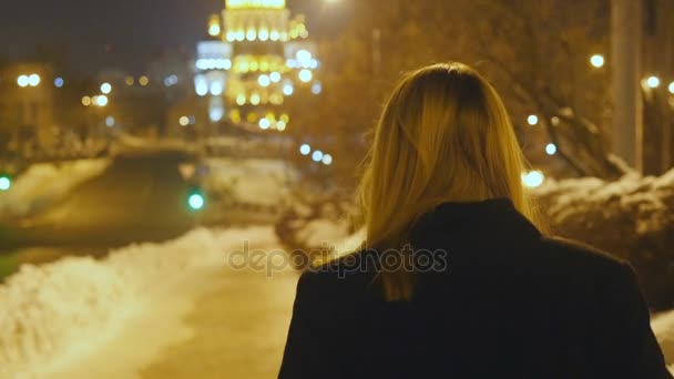 Молодая блондинка ходит по ночной зимней улице, наслаждаясь жизнью. Ночной город с огнями боке — стоковое видео