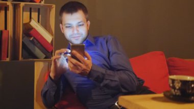 Genç yakışıklı bir fincan kahve için bir kafede oturur ve bir akıllı telefon kullanır