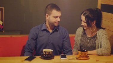 Konuşurken, bir kafede oturan bir çift içecekler kahve ve telefonu izliyor