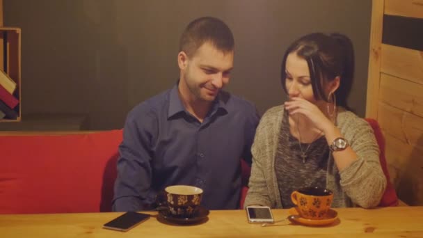 Una pareja sentada en un café, hablando, tomando café y mirando el teléfono — Vídeos de Stock