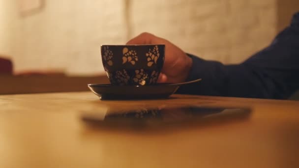 La mano del hombre toma una taza de café y bebida, luego toma el teléfono móvil del escritorio de madera. Concéntrate en la taza, luego en el teléfono. Primer plano — Vídeo de stock