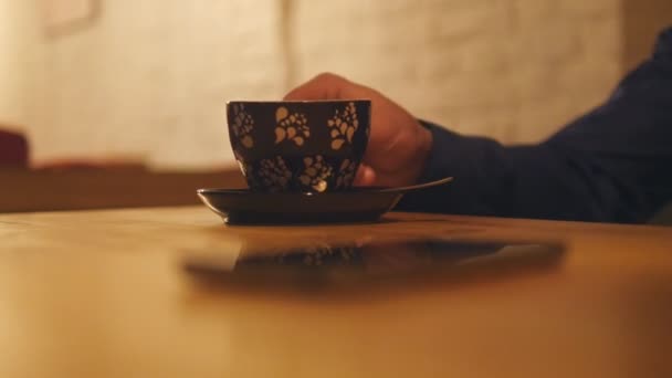 Man mão toma xícara de café e beber, em seguida, leva telefone celular de mesa de madeira. Concentra-te na chávena e depois no telefone. Close-up — Vídeo de Stock