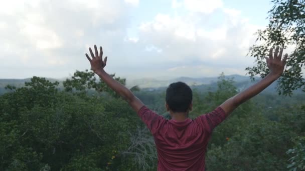 Little indian boy reaching up top of mountain and raised hands. Young man standing on the edge of beautiful canyon, victoriously outstretching arms up. Slow motion Rear back view — Stock Video
