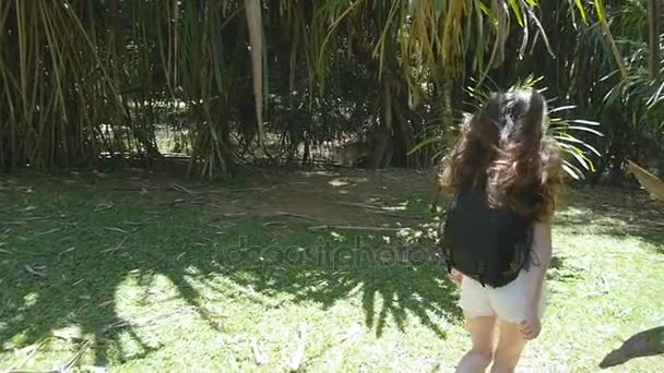 Happy girl with backpack is running along green jungle and having fun. Young beautiful woman jogging and spinning at tropical forest. Freedom travel concept Slow motion Rear back view — Stock Video