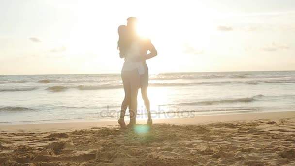 Счастливая пара целуется и обнимается на морском пляже на закате. Молодой человек и влюбленная женщина веселятся вместе на прекрасном берегу океана во время летних каникул или каникул. Медленное движение — стоковое видео