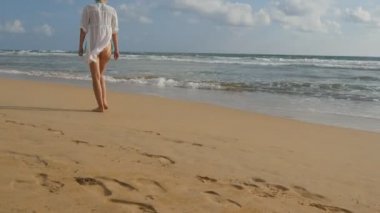 Mayo ve deniz kumsalda yalınayak yürüme gömlek güzel kadın. Okyanus kıyısında giden genç kız. Kum ile deniz dalgaları arka plan üzerinde adım ayak. Yaz tatil kavramı arkadan görünüş