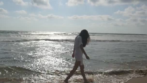 Ευτυχισμένη γυναίκα με μπικίνι και πουκάμισο περπάτημα πάνω στο νερό στην παραλία κοντά στον ωκεανό. Όμορφη κοπέλα απολαμβάνοντας τη ζωή και τη διασκέδαση στο κύμα της θάλασσας. Ή καλοκαιρινές διακοπές. Κοντινό πλάνο — Αρχείο Βίντεο