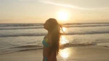 Okyanus kıyısında güneş doğarken poz uzun saçlı çekici seksi kız. Günbatımı üzerinde bikini duran deniz kenarında güzel genç kadın. Erkek sahilde tatil sırasında hayattan zevk. Yakın çekim