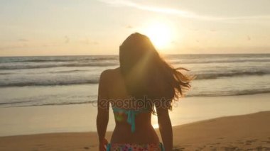 Günbatımı üzerinde bikini duran deniz kenarında güzel genç kadın. Okyanus kıyısında güneş doğarken poz uzun saçlı çekici seksi kız. Erkek sahilde tatil sırasında hayattan zevk. Yakın çekim