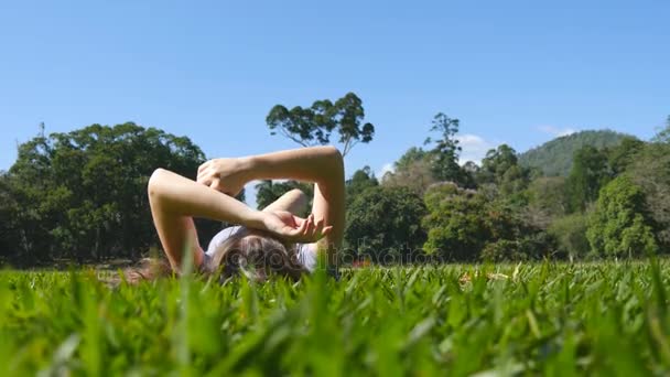 Νεαρή γυναίκα που βρίσκεται στο καταπράσινο γρασίδι στο πάρκο και χαλαρώνοντας. Κορίτσι που κάθεται στο Λιβάδι στην φύση, και βλέποντας τον ουρανό. Γυναίκα κοιτάζοντας το τοπίο και απολαμβάνουν διακοπές. Χαμηλή γωνία προβολής πίσω πίσω προβολή — Αρχείο Βίντεο