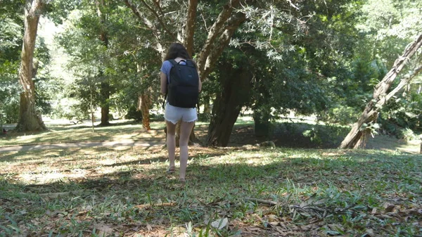 Turysta dziewczyna z plecaka jest chodzenie wzdłuż lasu tropikalnego. Kobiece stopy stepping w hill na drewno. Młoda kobieta wybiera się na zielony dżungli. Pojęcie wolności podróży. Widok z tyłu powrotem Close up — Zdjęcie stockowe
