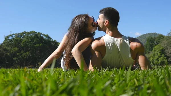 Giovane coppia sdraiata su erba verde nel parco e rilassante. Uomo e donna seduti sul prato a baciare la natura. Ragazza e ragazzo guardando il paesaggio e godendo di vacanza. Posteriore Indietro Angolo di vista basso — Foto Stock