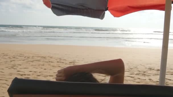 Jeune femme allongée sur un transat au bord de la mer et bronzant. Corps féminin sur chaise longue relaxant et profiter pendant les vacances d'été sur la plage de sable vide de l'océan. Une fille en bikini dans un resort. Gros plan — Video