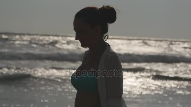 Profile of woman in bikini and shirt walking on the beach near the ocean at evening. Young beautiful girl enjoying life at sea shore. Summer vacation or holiday. Profile close up view — Stock Video