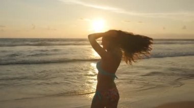 Okyanus kıyısında güneş doğarken poz uzun saçlı çekici seksi kız. Bikini ayakta deniz günbatımı güzel genç kadın. Erkek sahilde tatil sırasında hayattan zevk. Yakın çekim