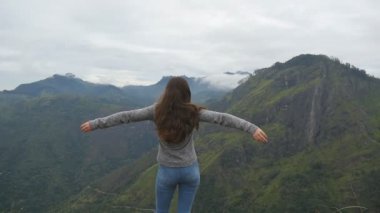 Dağ ve yükseltilmiş elleri yukarı ulaşan genç kız. Güzel Kanyon kenarında duran, zaferle yukarı silah outstretching kadın turist. Ağır çekim arka geri görüntülemek
