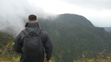 Genç erkek uzun yürüyüşe çıkan kimse dağ ve yükseltilmiş elleri yukarı ulaşan sırt çantası ile. Güzel Kanyon kenarında duran, zaferle yukarı silah outstretching adam turist. Ağır çekim arka geri görüntülemek