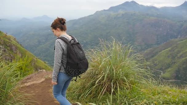 Молодая женщина турист с рюкзаком ходить по тропе в горах с красивым природным ландшафтом на заднем плане. Женщина-туристка идет вдоль узкого гребня на вершине хребта. Здоровый активный образ жизни. Медленное движение — стоковое видео