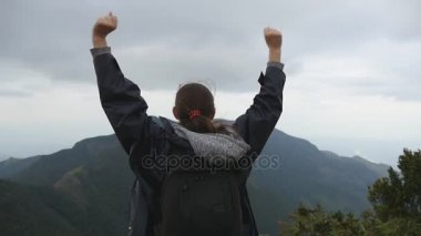 Güzel Kanyon kenarında duran, zaferle yukarı silah outstretching kadın turist. Genç kadın uzun yürüyüşe çıkan kimse dağ ve yükseltilmiş elleri yukarı ulaşan sırt çantası ile. Ağır çekim arka geri görüntülemek