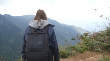 Genç kadın uzun yürüyüşe çıkan kimse dağ ve yükseltilmiş elleri yukarı ulaşan sırt çantası ile. Zaferle yukarı silah outstretching kadın turist yağmurluk ayakta güzel Kanyon kenarına. Ağır çekim