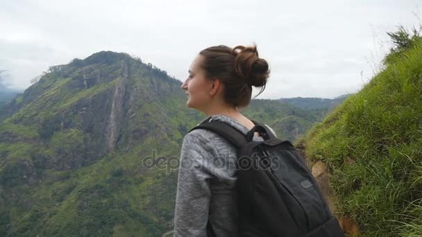 Jovem turista com mochila desfrutando de bela vista nas montanhas. Mulher viajante de pé na borda do belo desfiladeiro e olhando para a natureza. Lento movimento Fechar — Vídeo de Stock
