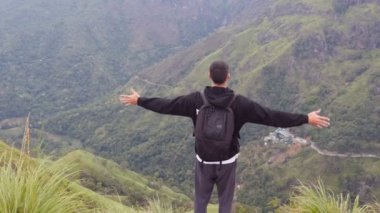 Genç turizm sırt çantası konumu güzel Kanyon kenarına olan adam ve zaferle ellerini kaldırdı. Dağın tepesine kadar ulaşan ve yukarı silah outstretching erkek uzun yürüyüşe çıkan kimse. Arka arkadan görünüm