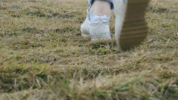 Foot of woman stepping up to the hill. Female legs in sneakers walking over green grass at the park. Low angle of view Close up — Stock Video