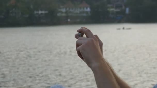 Mãos masculinas segurando smartphone e fotografando atrações da cidade com rio no fundo. Homem fazendo foto no telefone ao ar livre. Fechar — Vídeo de Stock