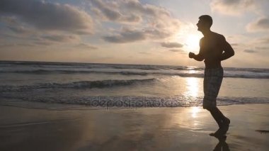 Atletik adam okyanus kıyı gündoğumu sırasında koşu. Deniz sahilde günbatımında çalışan sportif delikanlı. Açık egzersiz erkek sporcu. Sağlıklı aktif yaşam tarzı. Doğa, egzersiz. Ağır çekim